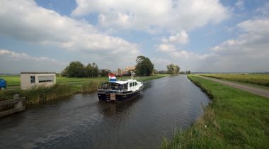 Foto van boot die vaart op sloot tussen landschap en weg