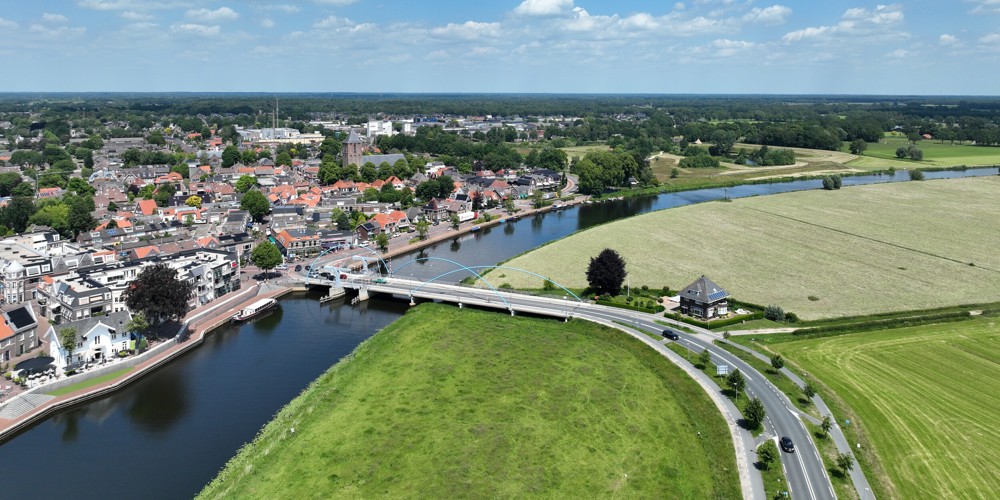 Een brug die over een brede rivier rijkt vanuit het landschap naar een stad
