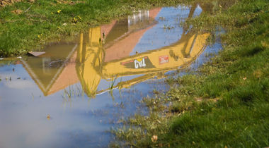 Plas in het gras met weerspiegeling van graafmachine en woning in plas