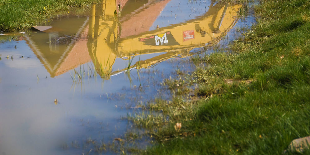 Plas in het gras met weerspiegeling van graafmachine en woning in plas