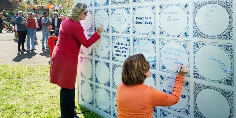 Twee vrouwen schrijven op een muur van grote, blauw-witte tegels tijdens Koningsdag 2025.
