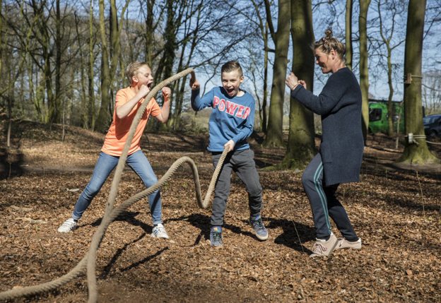 Kind die speelt met touwen in bos en toegejuicht wordt door twee personen om hem heen