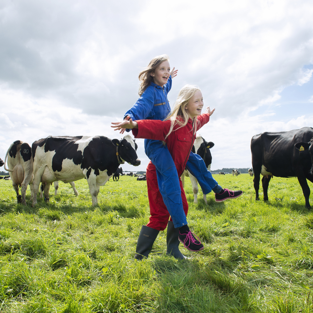 Foto van twee kinderen in overalls tussen koeien