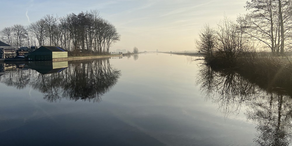 Kanaal bij het ochtendlicht met reflecterende bomen langs de rand in de winter