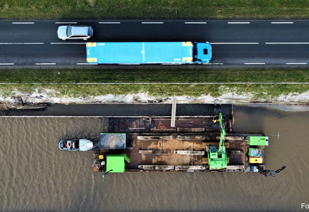Vogelperspectief van boot met graafmachines op rivier langs eenverkeersautoweg met auto en vrachtwagen
