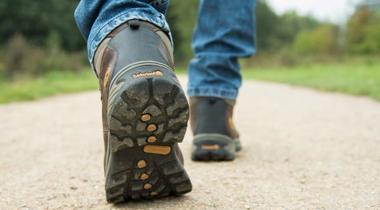 Onderbenen van een man met werkschoenen aan die loopt op een grindpad