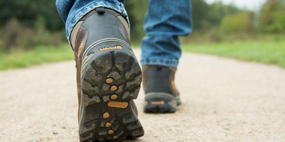 Onderbenen van een man met werkschoenen aan die loopt op een grindpad