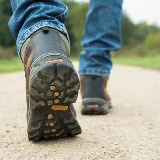 Onderbenen van een man met werkschoenen aan die loopt op een grindpad