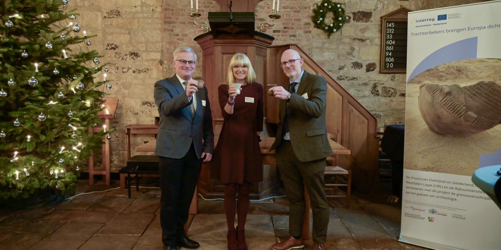 Gert Harm ten Bolscher, Frau Dr. Barbara Rüschoff-Parzinger, hoofd culturele zaken van de projectpartner Landschaftsverband Westfalen-Lippe (LWL) en Mike Rose (funding officer van de Rijksuniversiteit Groningen) brengen een toost uit met een trechtbeker in de hand.