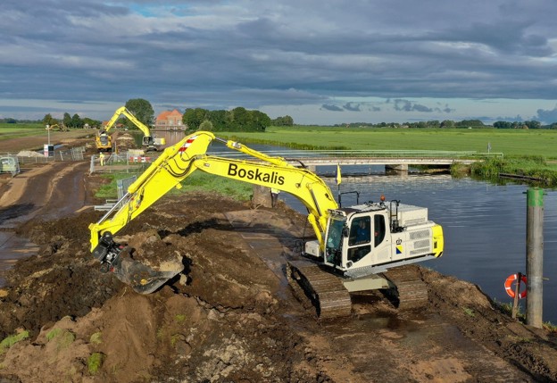 Gele graafmachine tussen zandgrond naast brug en sloot
